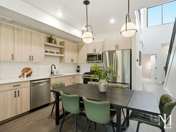 Modern kitchen and dining area with light wood cabinetry, stainless steel appliances, and vaulted ceiling.