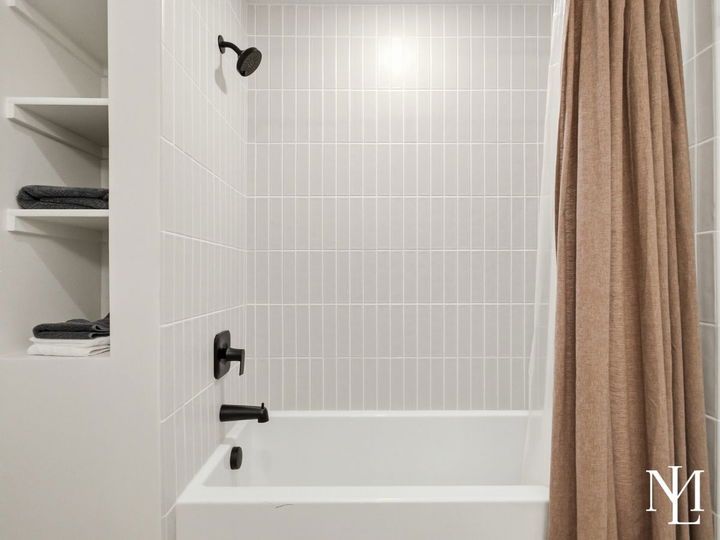 Bathroom with white tile shower and tub, black fixtures, and built-in linen shelving.