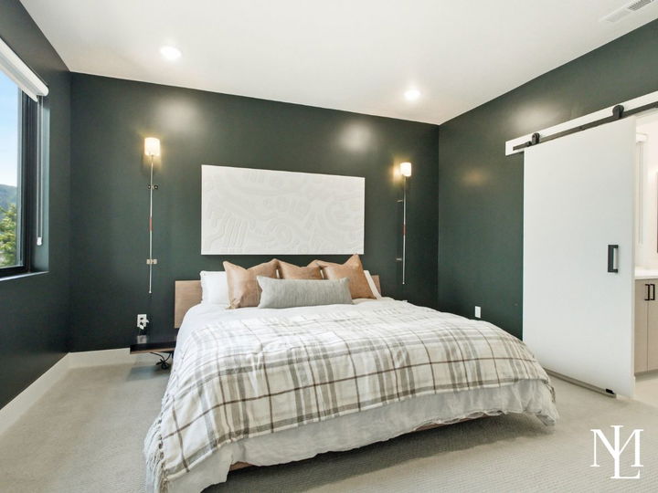 Bedroom with dark accent wall, sliding barn door, wall sconces, and en suite bathroom access.