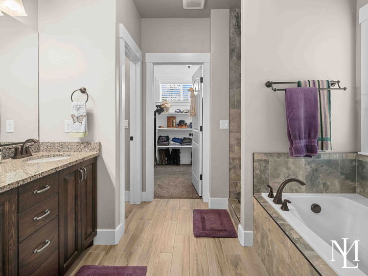 Primary bathroom with granite vanity, soaking tub, tile flooring, and walk-in closet access.