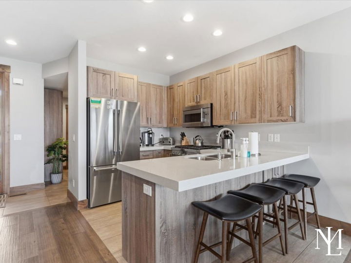 Modern kitchen with wood cabinetry, quartz island, stainless appliances, and bar seating.