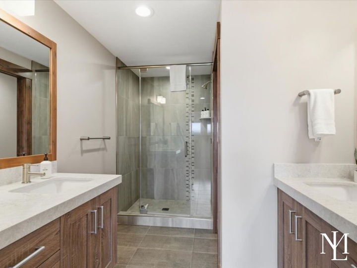 Bathroom with dual vanities, wood cabinetry, and glass walk-in shower.