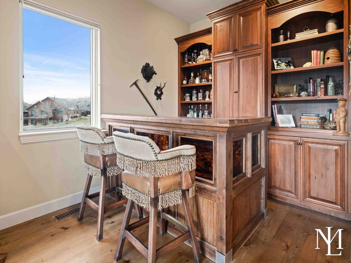 Built-in bar with warm woods and two upholstered stools with fringe