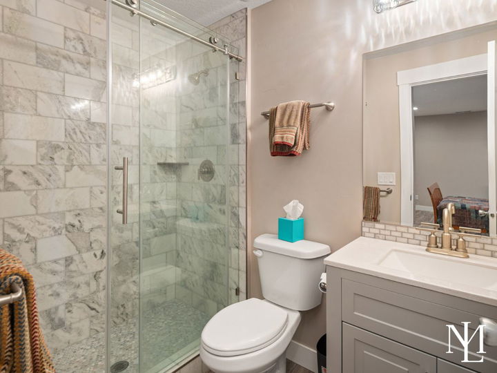 Bathroom with marble tile walk-in shower, vanity, mirror, and neutral finishes.