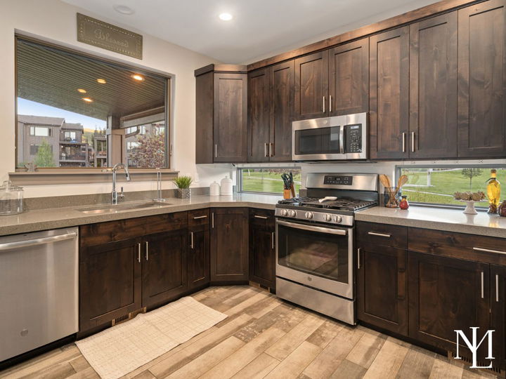 Kitchen with dark wood cabinetry, stainless steel appliances, and windows overlooking the covered deck.