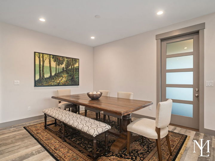 Dining room with wood table, upholstered seating, patterned rug, and modern glass door.
