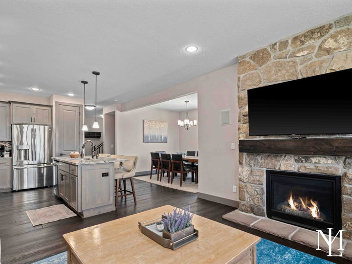 Open living area with stone fireplace, kitchen, dining space, dark wood flooring, and warm mountain-modern finishes.