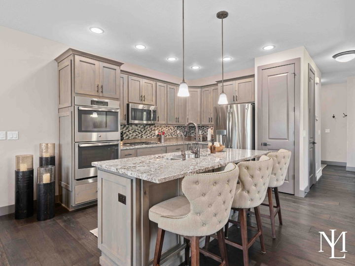 Updated kitchen with granite island, gray cabinetry, stainless steel appliances, pendant lighting, and bar seating.