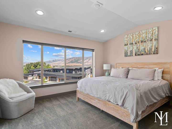 Primary bedroom with large picture window, mountain views, soft neutral furnishings, and natural light.