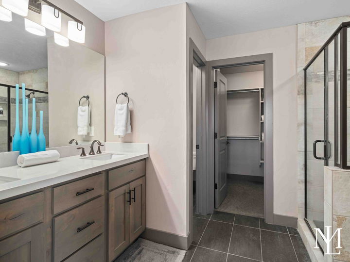 Primary bathroom with glass shower, vanity, walk-in closet access, and modern tile finishes.