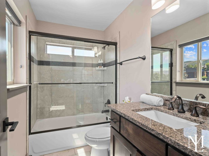 Full bathroom with tub-shower combo, granite vanity, tile surround, and mountain views through the window.