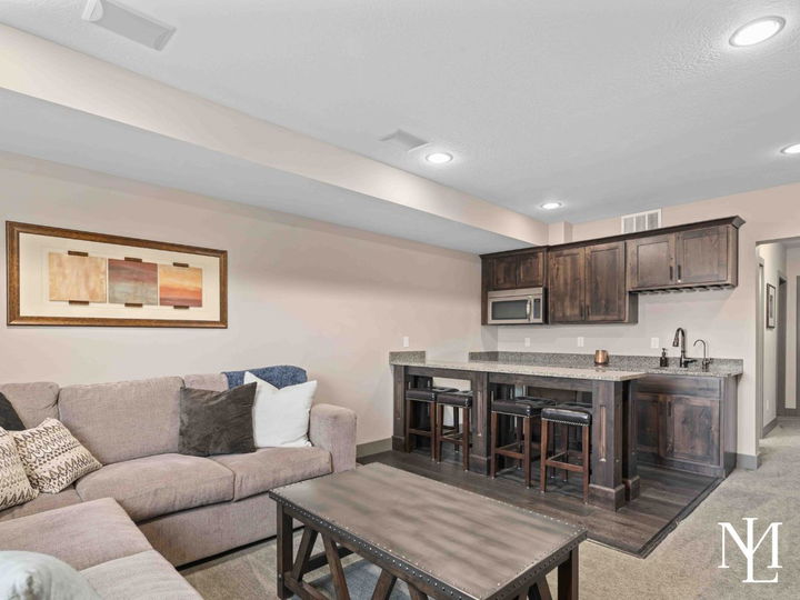 Finished lower-level family room with sectional seating, wet bar, dark cabinetry, and built-in microwave.