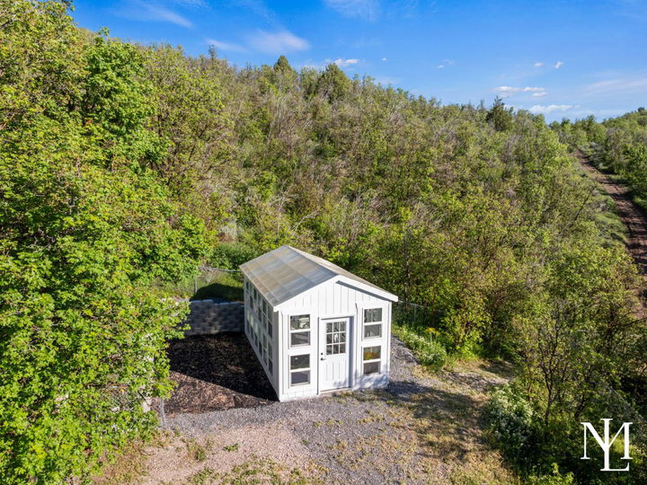 Custom greenhouse tucked into a wooded hillside setting with garden space and natural surroundings.