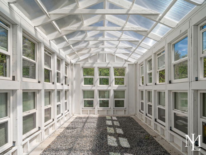Interior of a bright greenhouse with rows of windows, translucent roof panels, and gravel flooring.