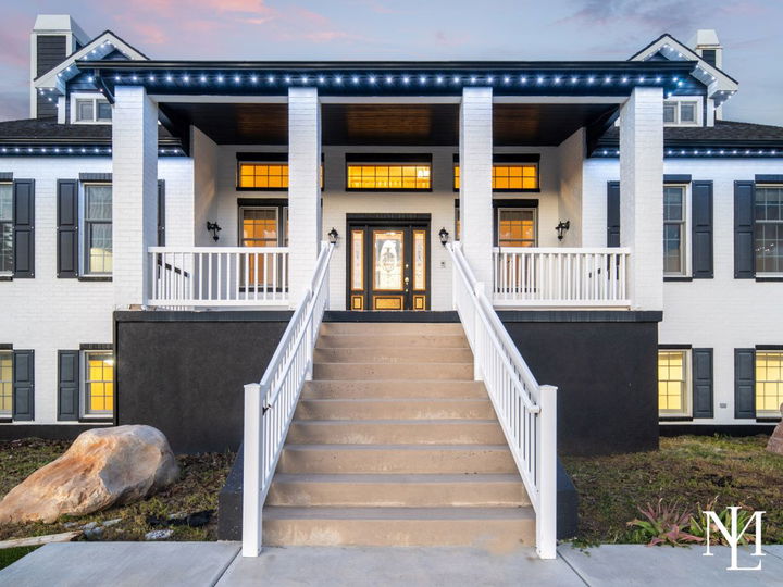Front entry of a white brick Huntsville home with grand staircase, covered porch, black shutters, and warm evening lighting.