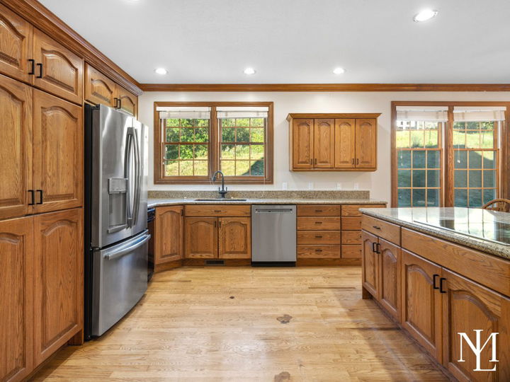 Spacious kitchen with wood cabinetry, granite countertops, stainless steel appliances, and large windows overlooking the property.