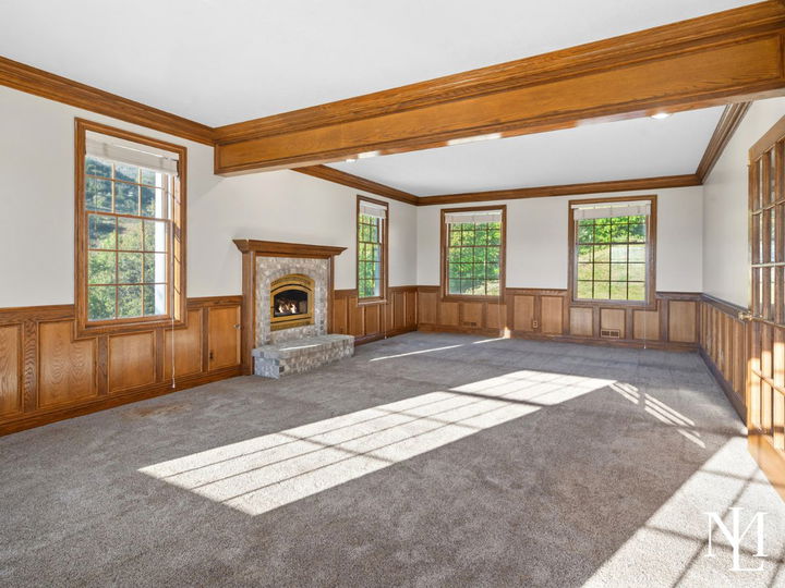 Formal living room with wood trim, fireplace, large windows, and natural light in a classic Huntsville mountain home.