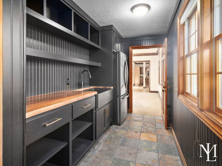 Updated mudroom or utility space with black cabinetry, wood countertops, slate tile flooring, and built-in storage.