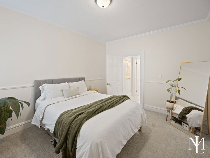 Neutral bedroom with carpet flooring, white bedding, full-length mirror, and clean finishes