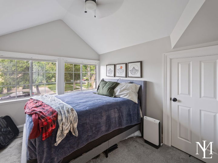 Upstairs bedroom with vaulted ceiling, large windows, carpet flooring, and cozy natural light
