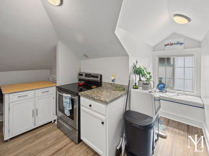 Compact kitchenette in Avenues triplex with white cabinetry, granite countertop, stove, and window seat