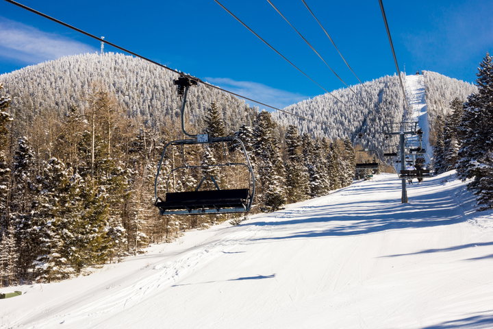 An empty chairlift silhouetted by snow covered pines in the morning at Angel Fire Resort in New Mexico.