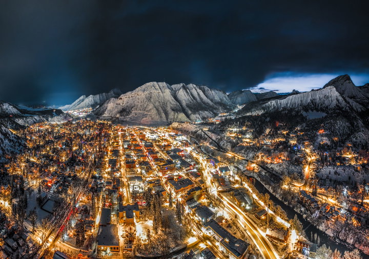 A stunning winter night aerial of Durango, Colorado, showcasing a glowing downtown wrapped in snow-covered mountains.