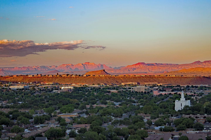 Evening view of St. George, Utah, with residential areas in the foreground and the red cliffs of the desert landscape illuminated by the setting sun in the background.