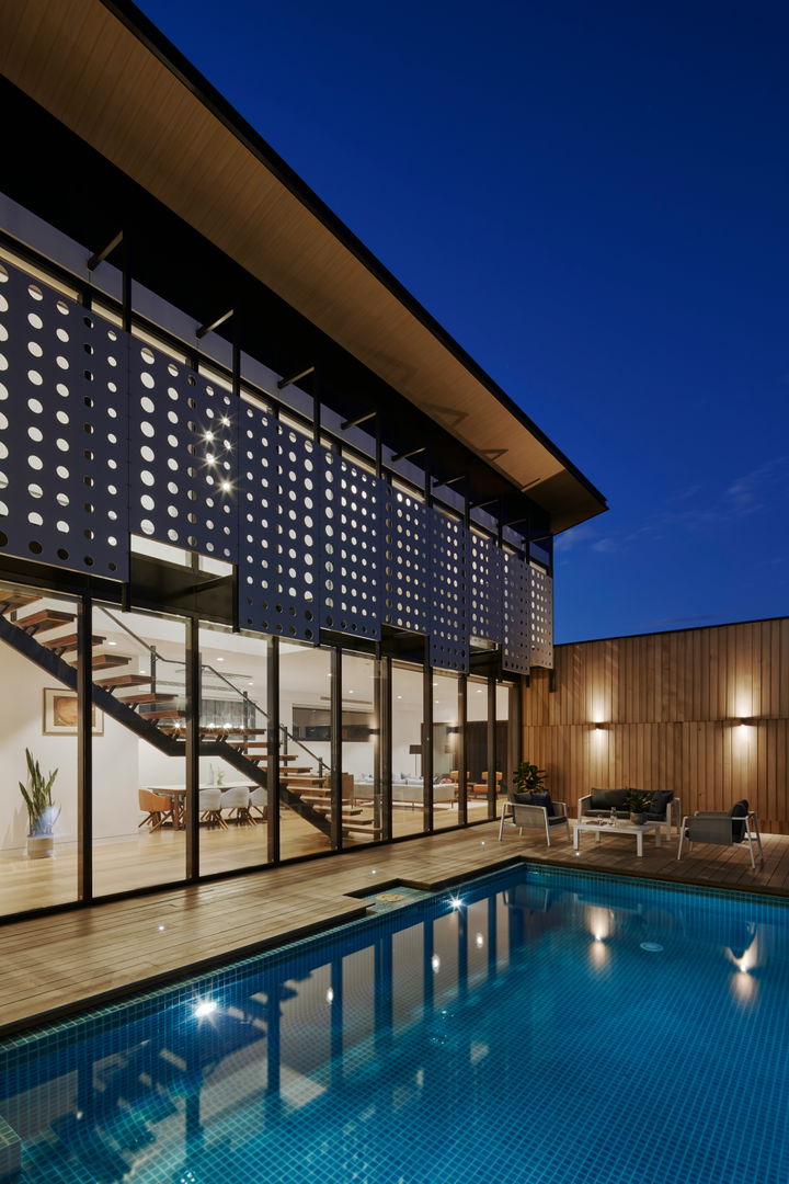 Outdoor lighting and a modern home interior illuminates a private pool and lounge area.