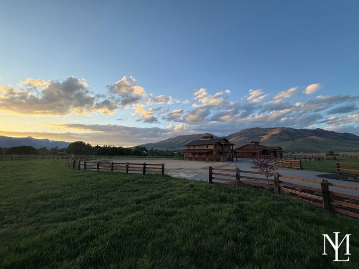 Wide view of a fenced horse property with barn, turnout area, and mountain backdrop during golden hour.