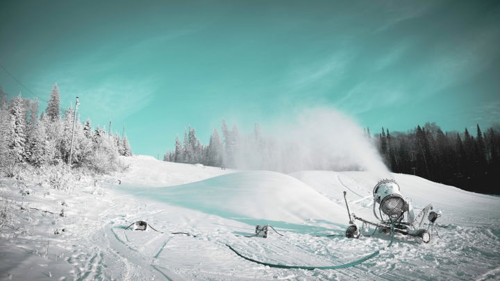 Groomer/snowmaking operations with mountain backdrop