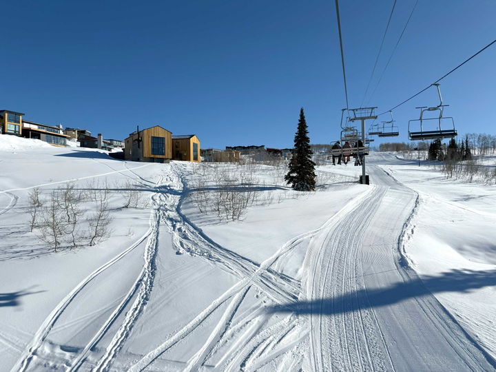 Modern cabin with ski in ski out access to a ski lift with 3 skiers on a blue bird day